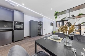 Une cuisine moderne dotée d’appareils électroménagers intégrés, un coin repas avec une table dressée pour deux personnes et une plante décorative dans un coin.