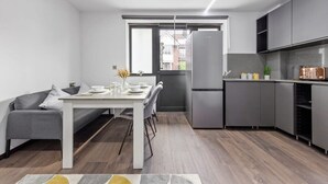 Una cucina moderna con mobili grigi, un frigorifero in acciaio inossidabile e un'area pranzo con tavolo bianco e divano grigio.