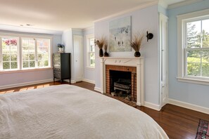 A spacious bedroom with a large bed, a fireplace, and a view of the outdoors through large windows. - Berkeley Home w/ Garden, Close to San Francisco! (Berkeley)