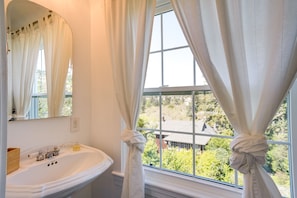 A bathroom with a white sink, a mirror, and a window with curtains tied back. - Berkeley Home w/ Garden, Close to San Francisco! (Berkeley)