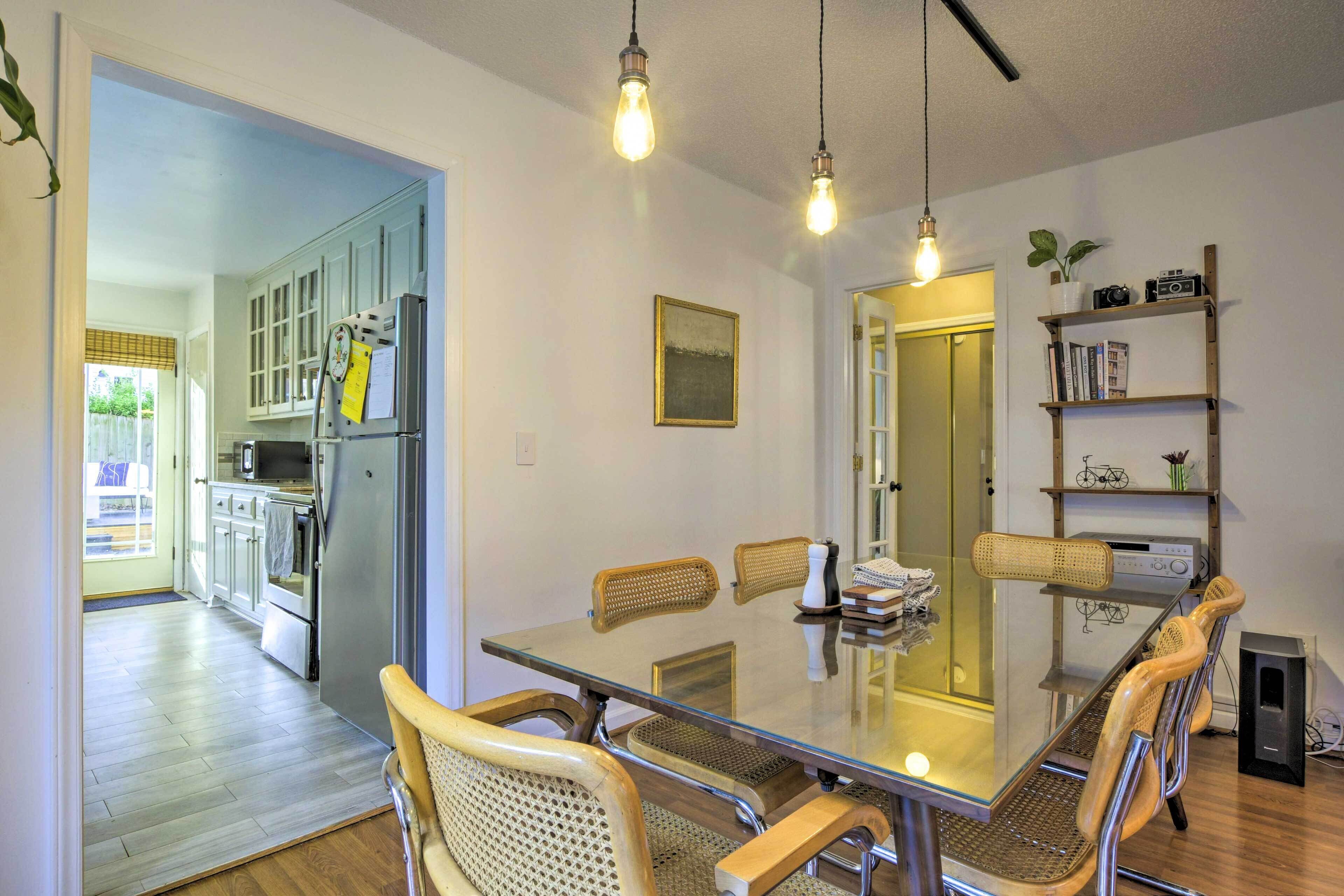 A dining area with a glass table, woven chairs, and a kitchen in the background.
