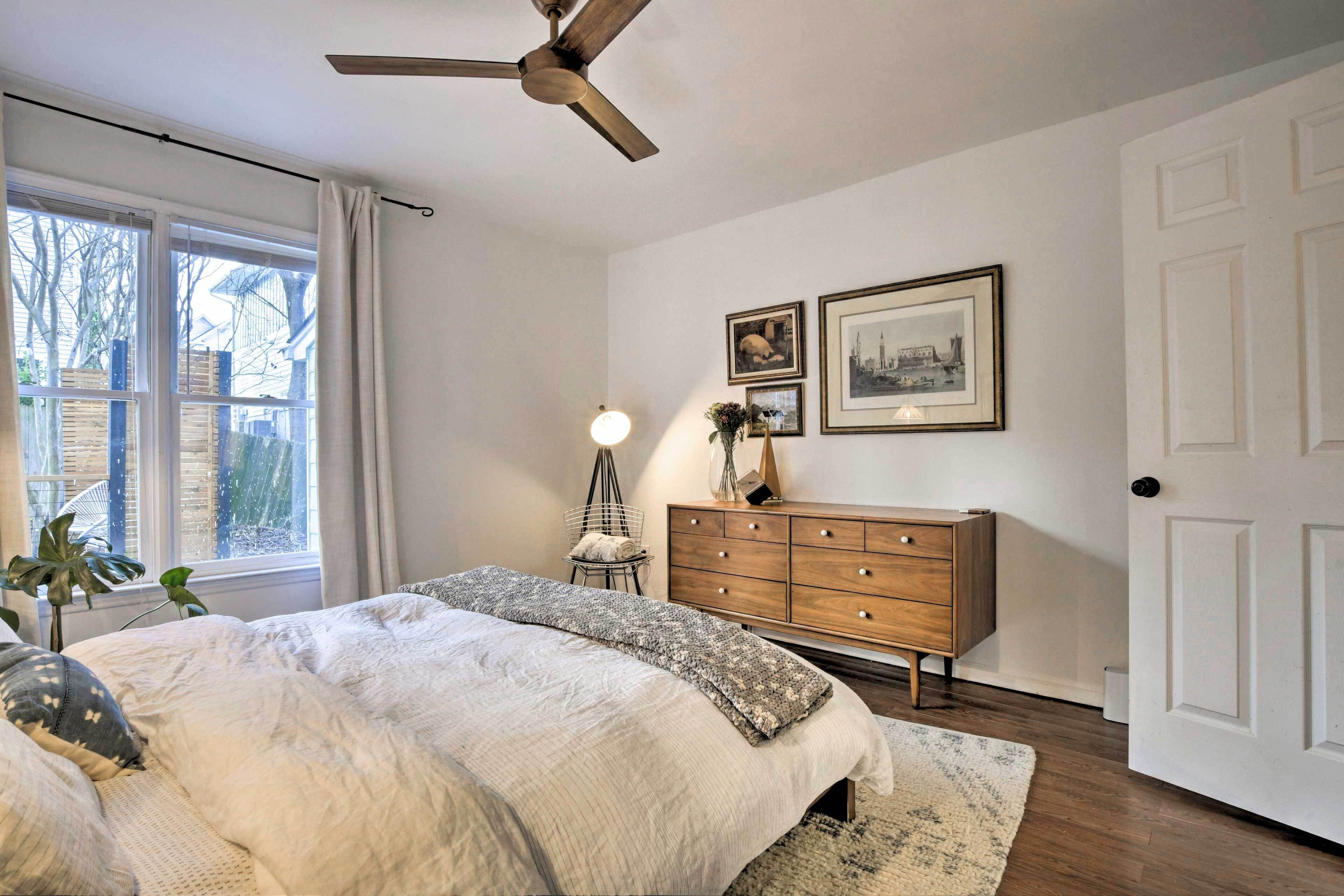 Een slaapkamer met een bed, een dressoir, een plafondventilator en een raam met gordijnen.