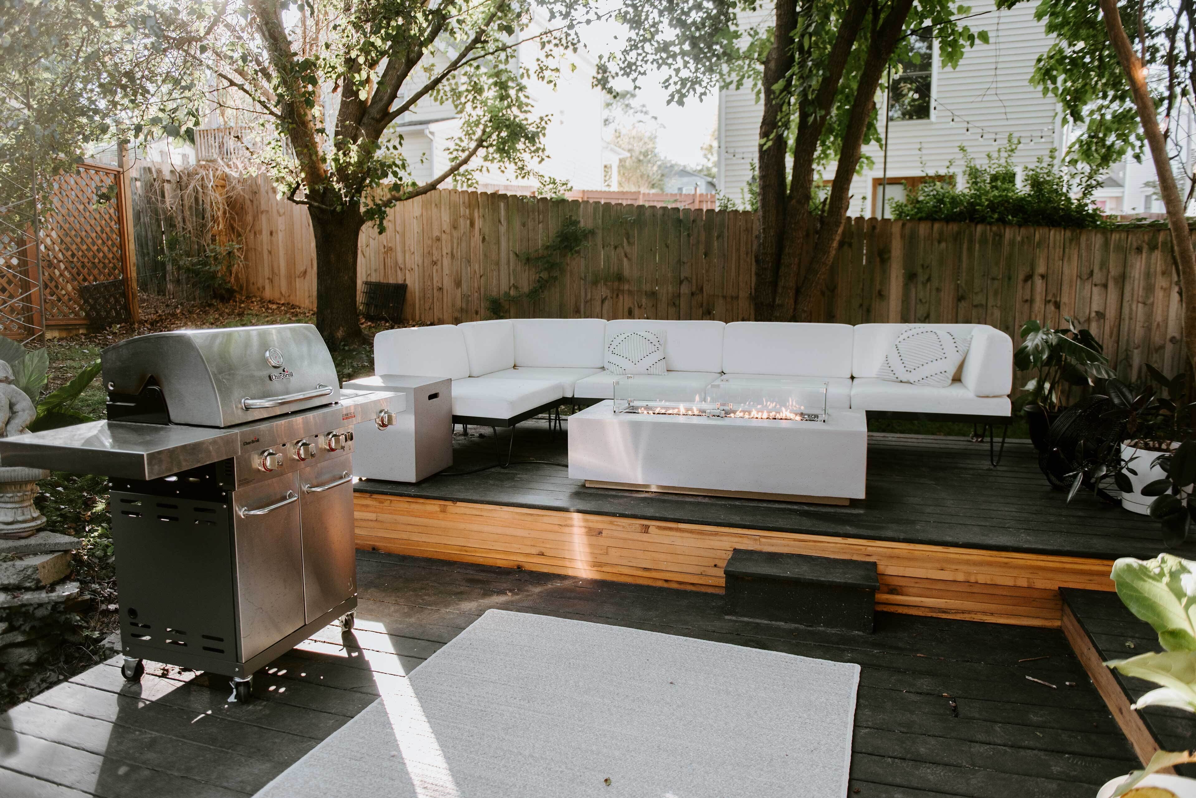 A backyard with a white sectional sofa, a grill, and a fire pit.
