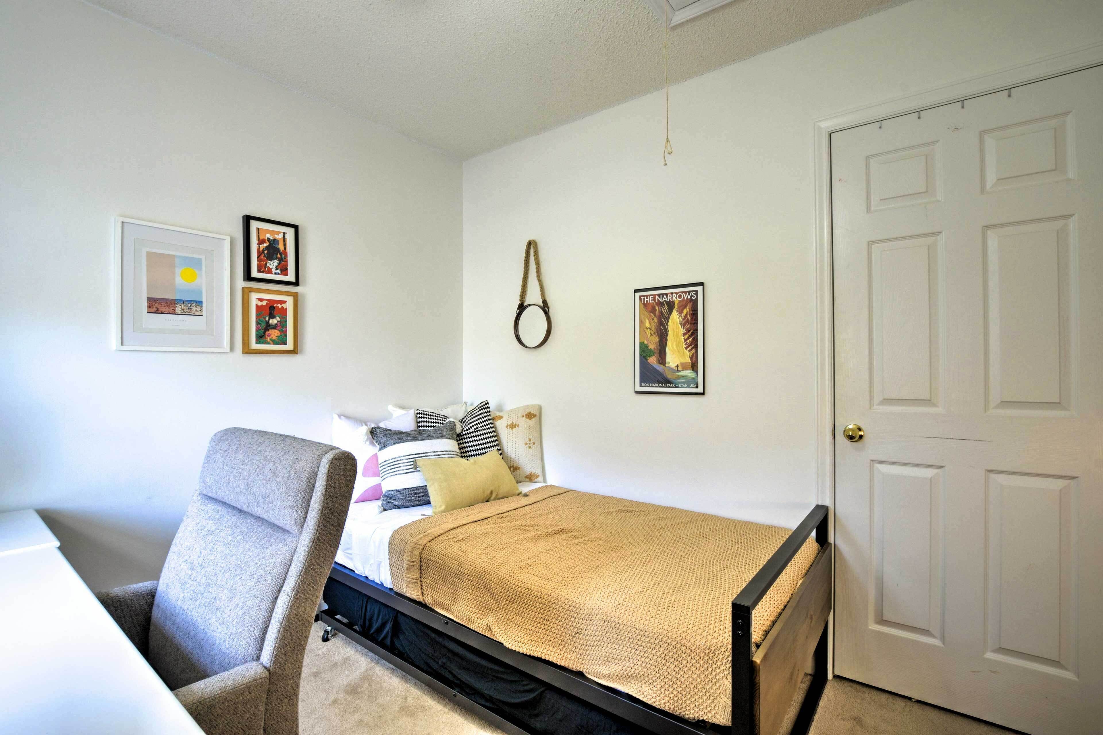 A bedroom with a bed, a chair, and a door. There are framed pictures on the wall.