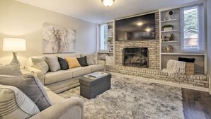 A living room with a fireplace, a sofa, a coffee table, and a TV mounted on the wall. - Renovated Raleigh Retreat w/ Patio in North Hills! (Raleigh)