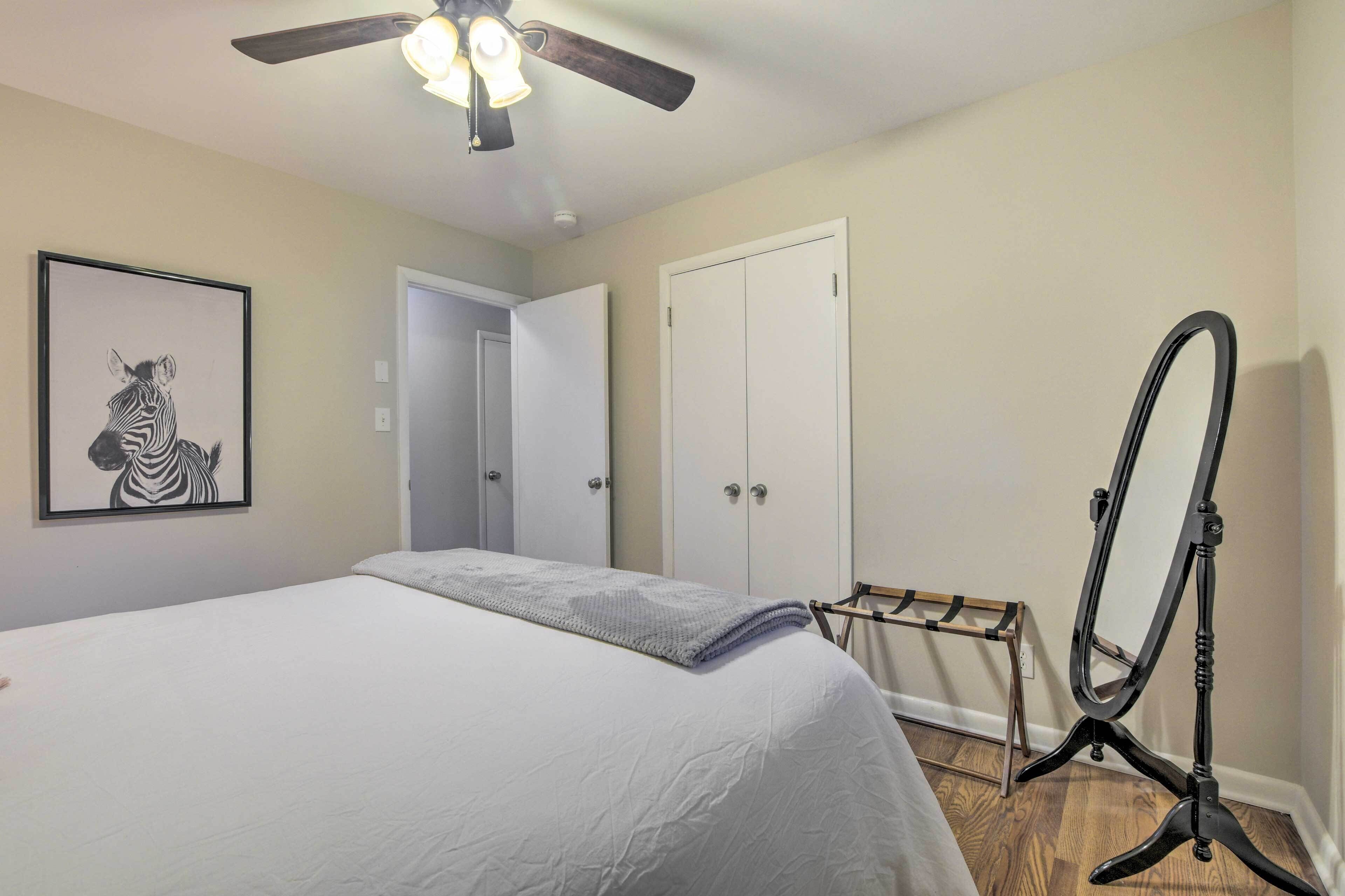A bedroom with a bed, a ceiling fan, a zebra artwork, a wardrobe, and a mirror stand.