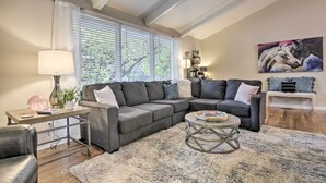 A modern living room with a sectional sofa, a round coffee table, and a large window with blinds. - Renovated Raleigh Retreat w/ Patio in North Hills! (Raleigh)