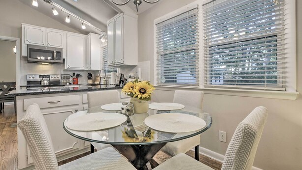 A modern kitchen with white cabinets, a glass dining table, and a view of the outdoors through large windows. - Renovated Raleigh Retreat w/ Patio in North Hills! (Raleigh)