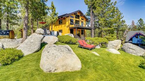 Une cabane en bois à deux étages, dotée d’un balcon, entourée de gros rochers et de pins.
