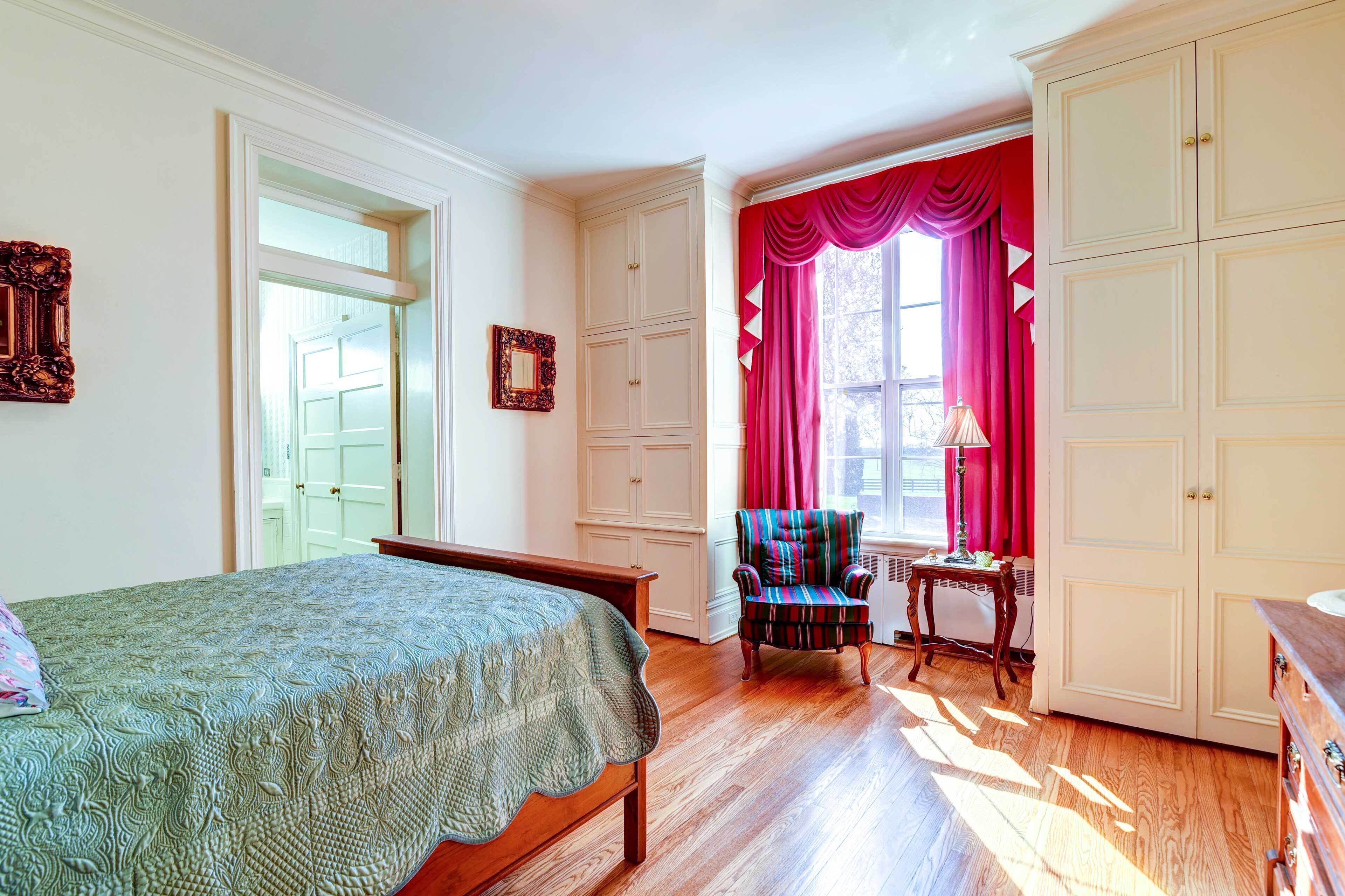 A bedroom with a bed, a chair, a dresser, and a window with curtains.