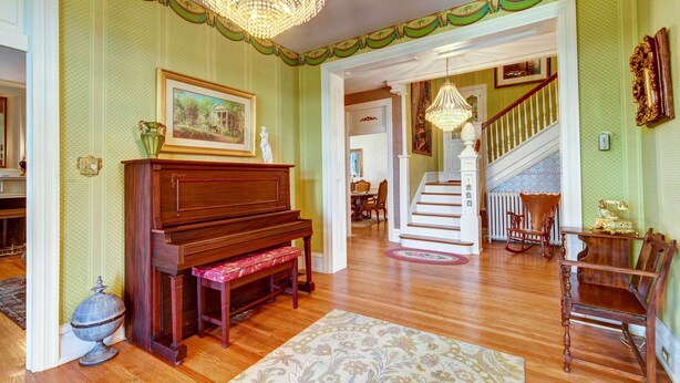 A spacious living room with a grand piano, a chandelier, and a staircase leading to another level. - Jennys Southland Homestead, LLC (Oakland)