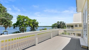 Un balcon donnant sur un lac et des arbres, avec une balustrade blanche et un bâtiment à la façade de couleur claire.