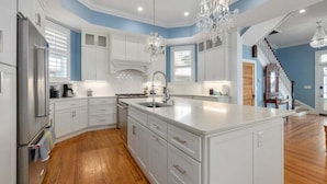 Une cuisine moderne avec des meubles blancs, un grand îlot central et un lustre.