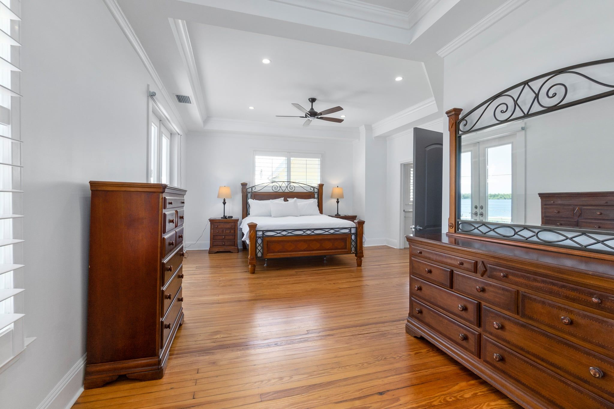 A spacious bedroom with a large bed, wooden dresser, and a ceiling fan.