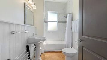 Une salle de bain avec une baignoire, deux lavabos, des toilettes et un rideau de douche.