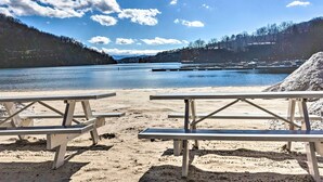 A beach with picnic tables and a calm lake. - Luxe Rumbling Bald Home w/ Deck & Mountain View (Lake Lure)