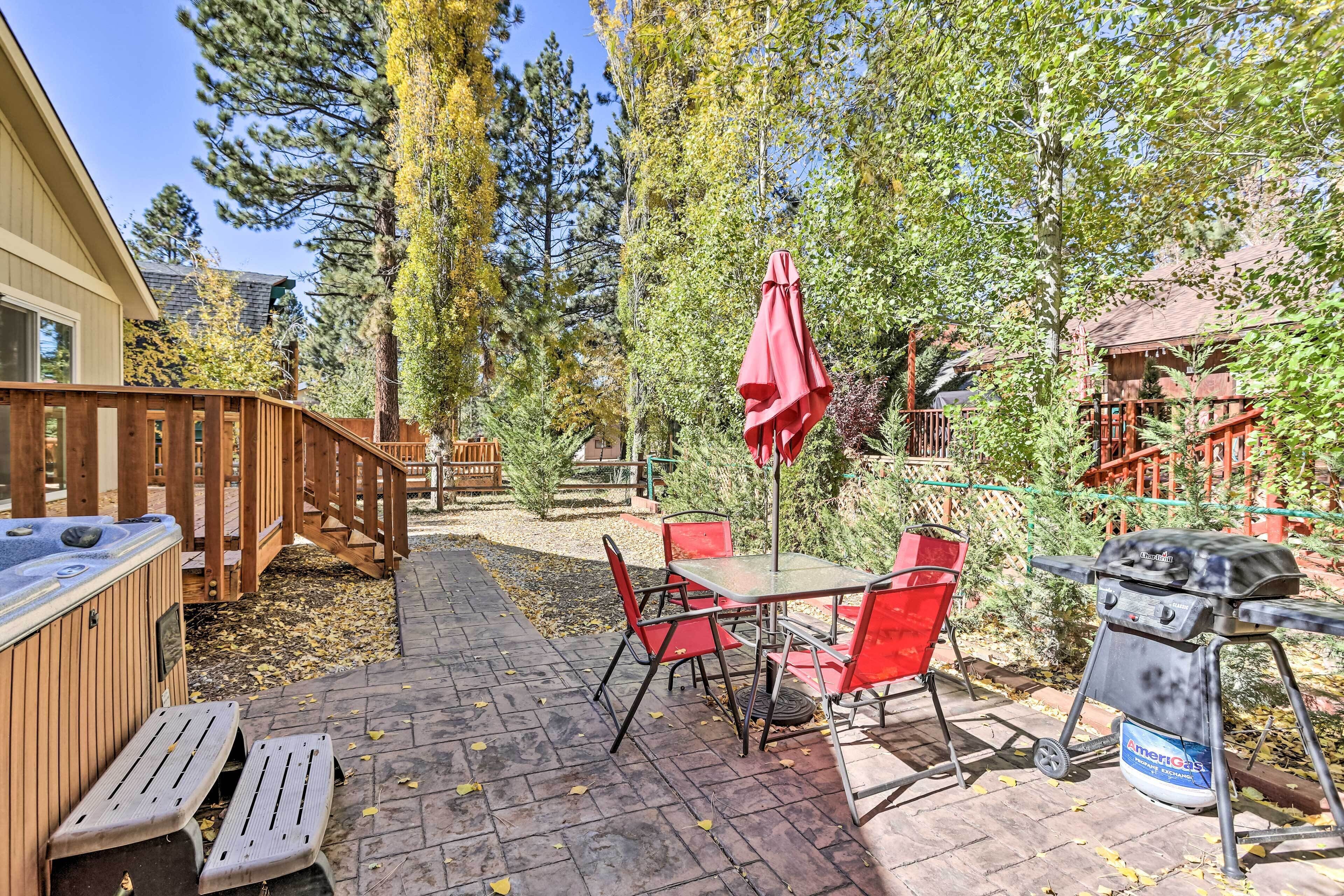 A patio with a hot tub, red chairs, and a grill.