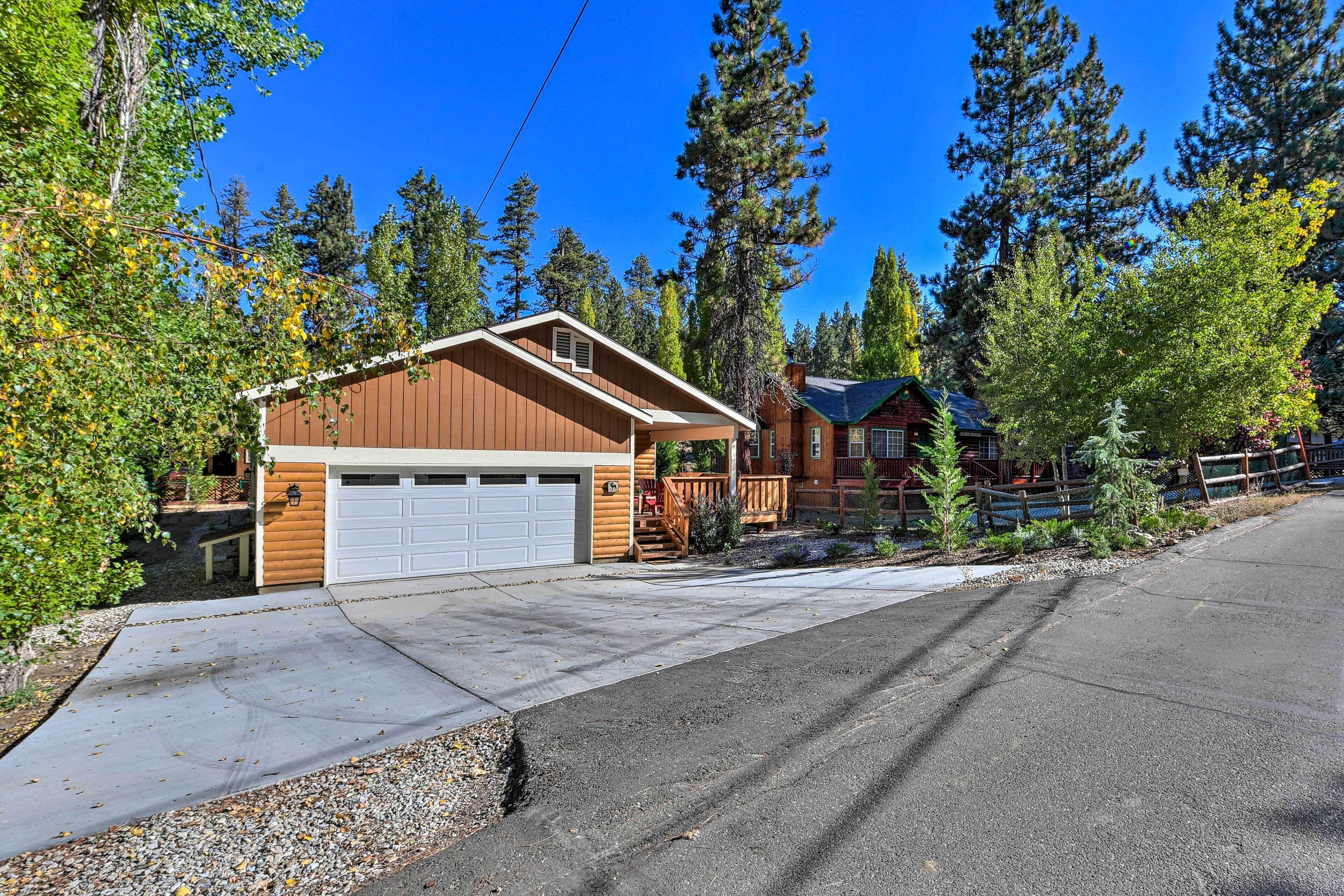 A two-story cabin with a garage, surrounded by tall trees and a clear blue sky.