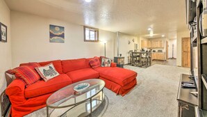 A living room with a red sectional sofa, a glass coffee table, and a kitchen in the background. - Priest Lake Apartment Near Hiking Trails! (Priest River)