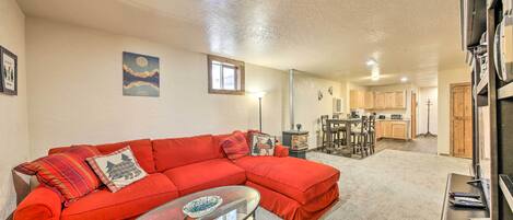 A living room with a red sectional sofa, a glass coffee table, and a kitchen in the background.