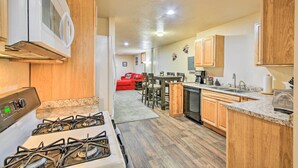 A kitchen with a gas stove, wooden cabinets, a microwave, and a dining area with a red sofa and chairs. - Priest Lake Apartment Near Hiking Trails! (Priest River)