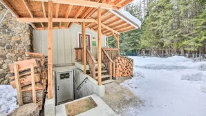 A covered wooden structure with a stone wall, a door, and a staircase leading to a wooden deck. - Priest Lake Apartment Near Hiking Trails! (Priest River)
