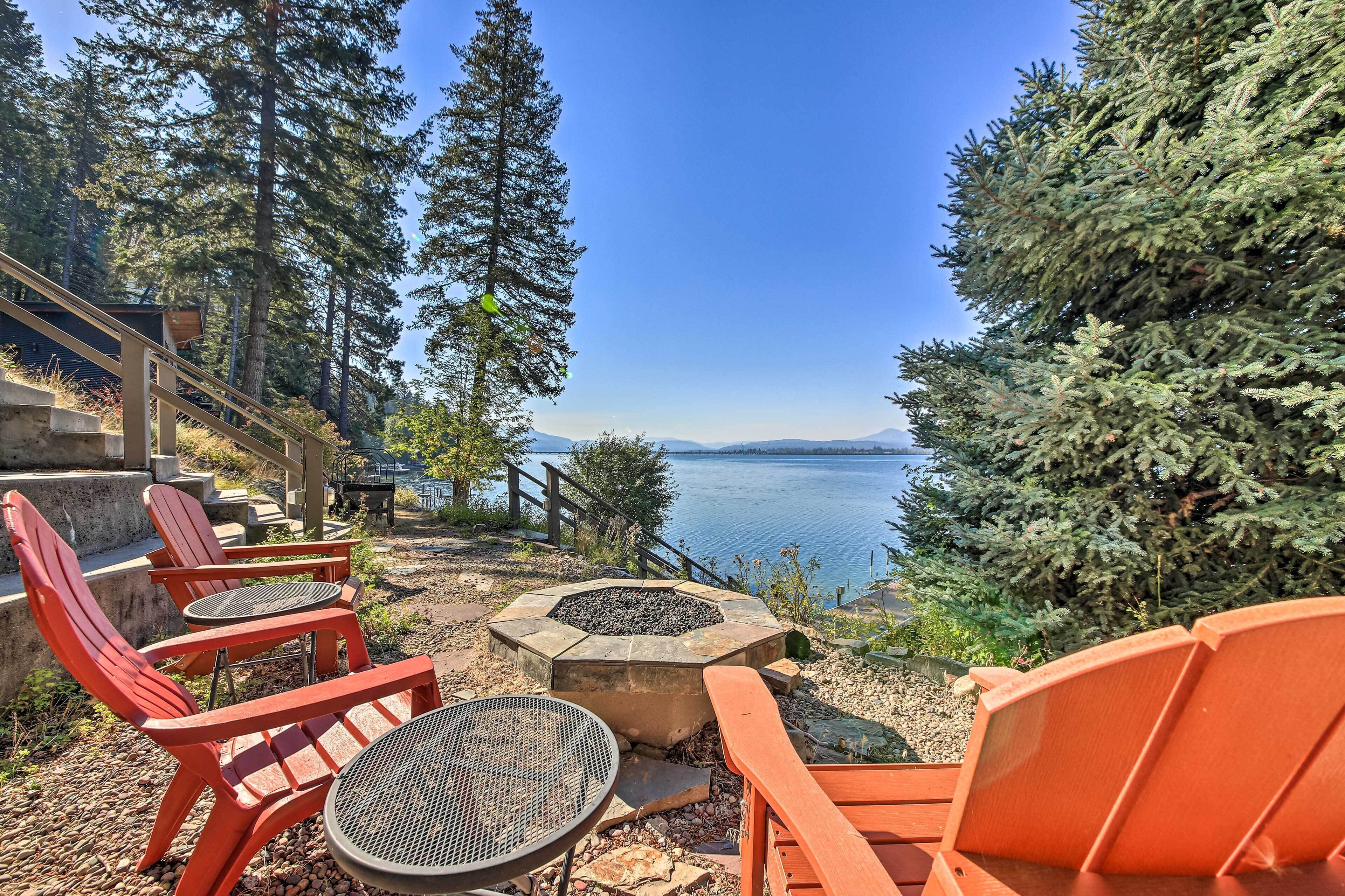 Une terrasse avec coin salon extérieur, un foyer et une vue sur un lac et des montagnes.
