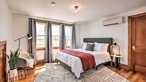 Une chambre avec un grand lit, une table de chevet, une lampe, une plante en pot et une vue sur l’extérieur par la fenêtre.