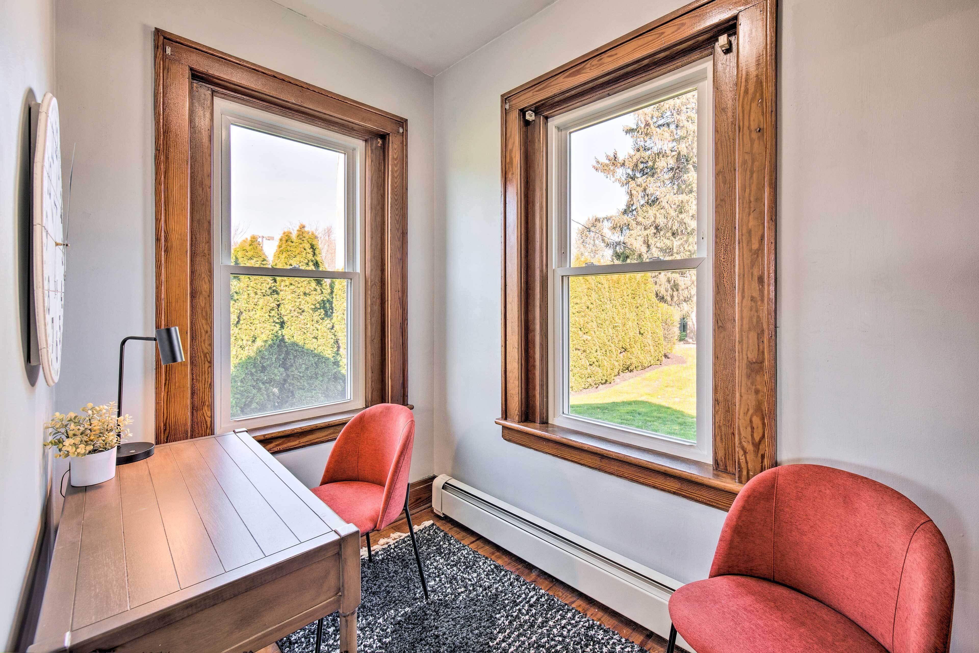 Une pièce avec deux fenêtres, un bureau, deux chaises, un radiateur et une plante en pot.