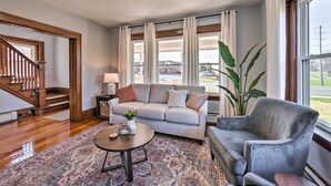 Un salon avec un canapé gris, une table basse ronde, un fauteuil gris, un tapis à motifs et une grande plante.