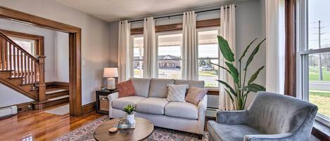A living room with a grey sofa, a round coffee table, a grey armchair, a patterned rug, and a large plant.