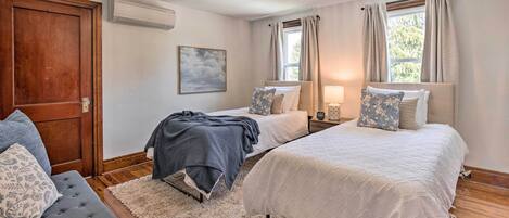 Ein Schlafzimmer mit zwei Betten, einer Holztür, einer Klimaanlage und einem Fenster mit Vorhängen.
