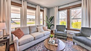 Un salon comprenant un canapé, des fauteuils, une table basse et de grandes fenêtres avec des rideaux.
