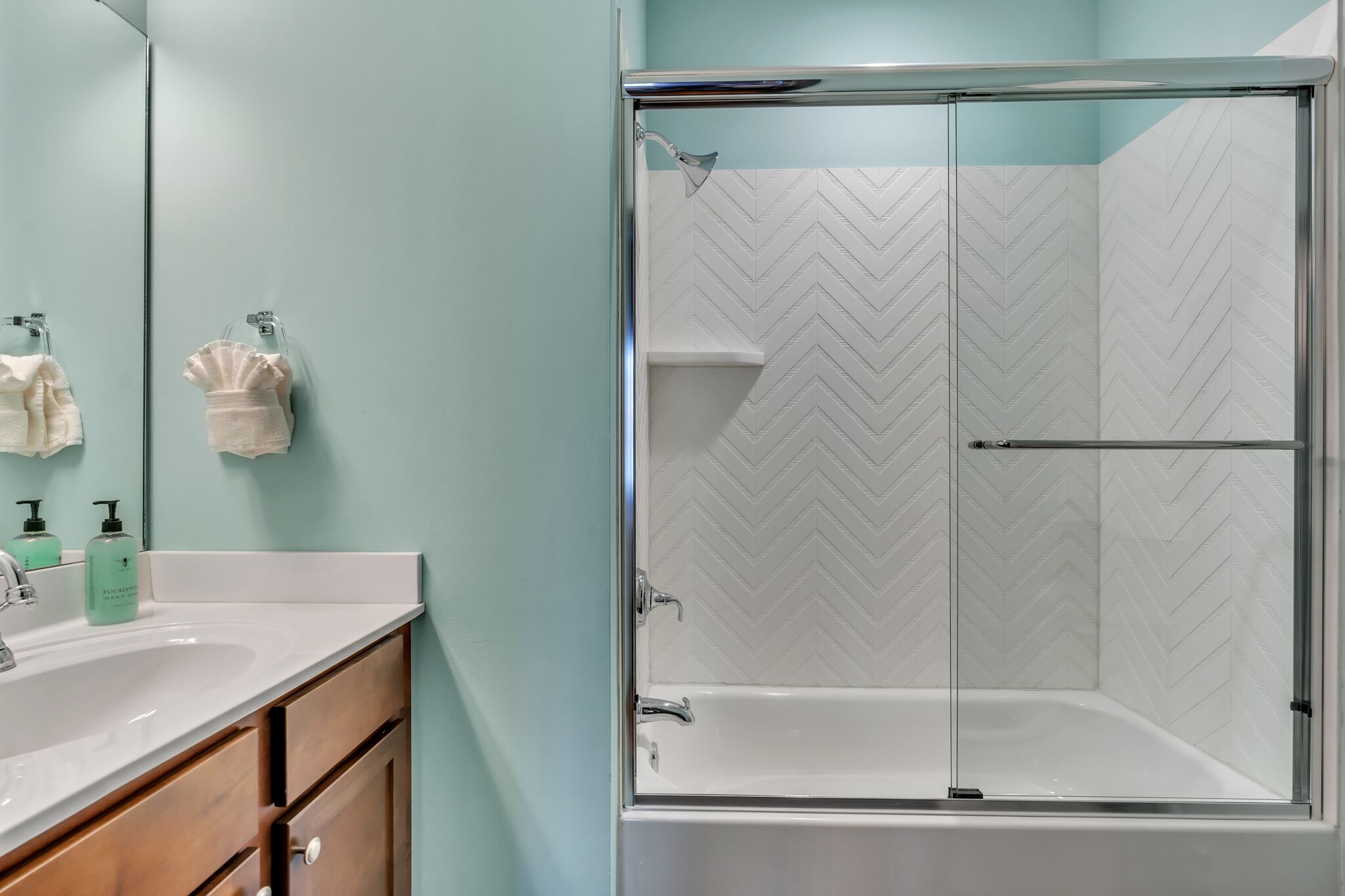 A modern bathroom with a glass-enclosed shower, a white sink, and a mirror.