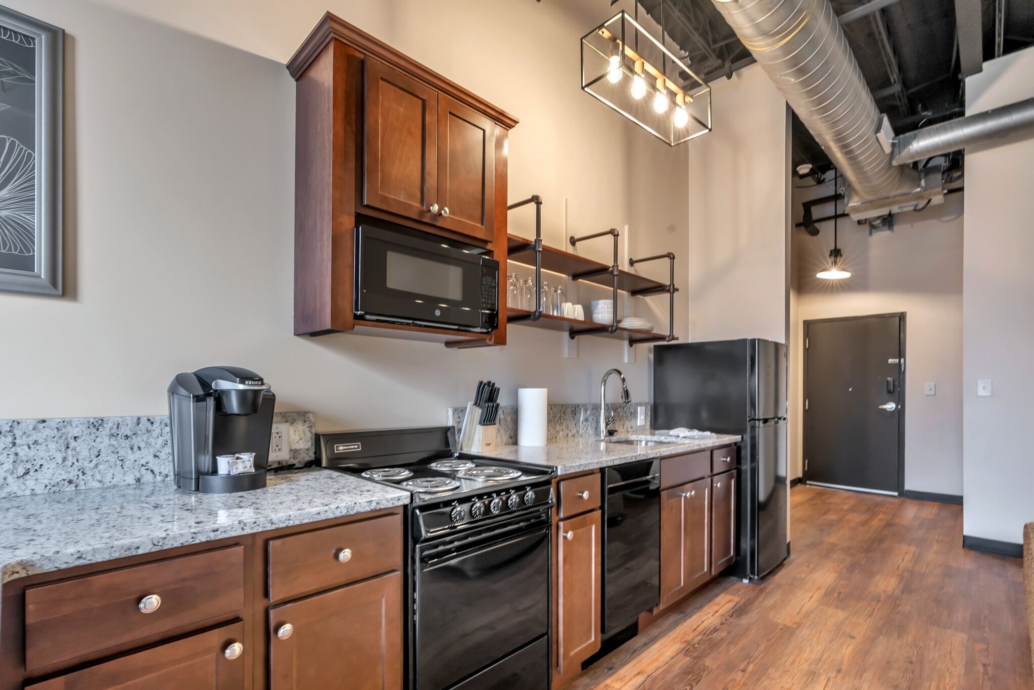 A modern kitchen with wooden cabinets, a built-in microwave, a coffee maker, and stainless steel appliances.