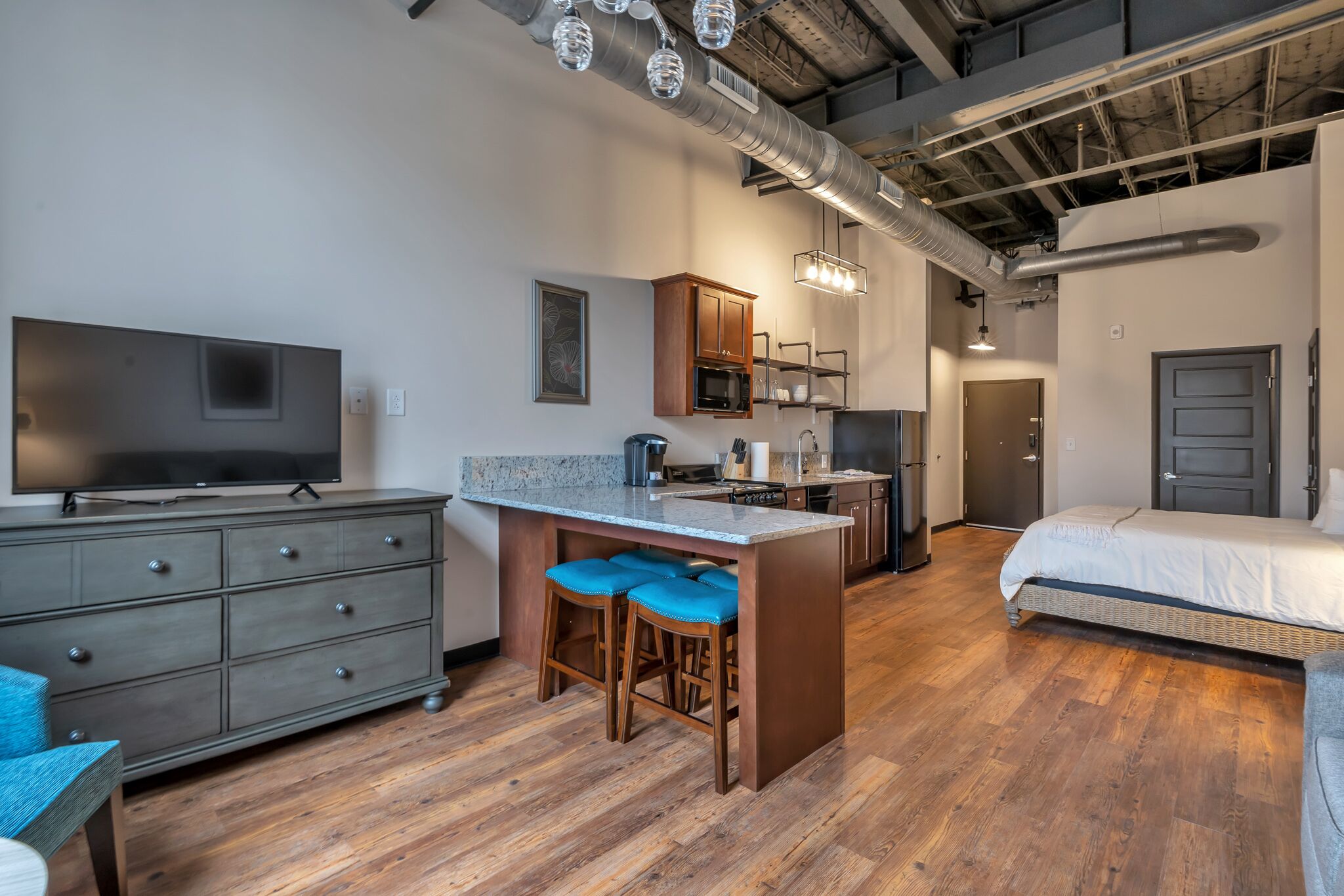 A modern kitchen with a central island, bar stools, a flat-screen TV, and built-in appliances.