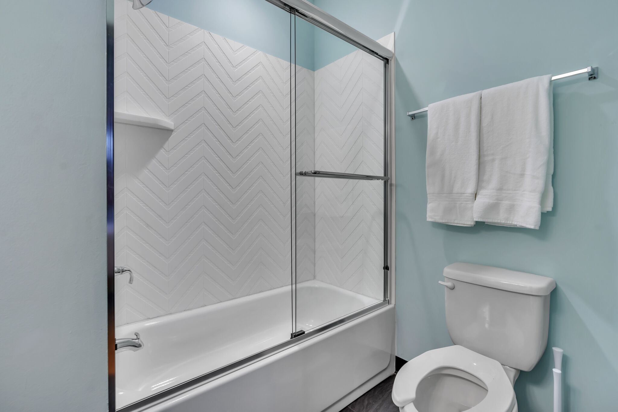 Ein Badezimmer mit einer gläsernen Duschkabine, einer weißen Toilette und einem Handtuchhalter mit zwei weißen Handtüchern.