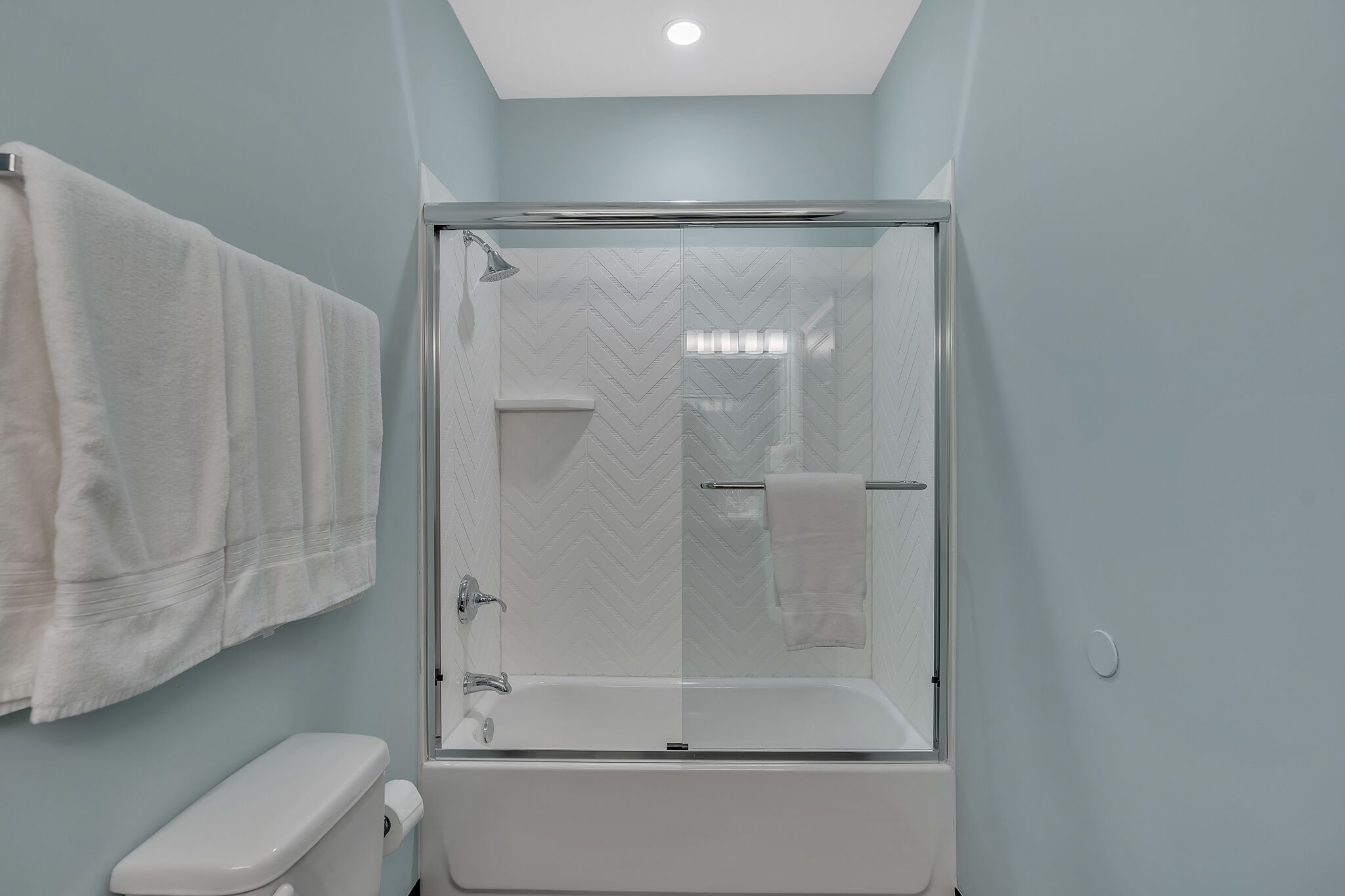Une salle de bain moderne avec une douche à parois de verre, des toilettes blanches et une serviette accrochée au mur.
