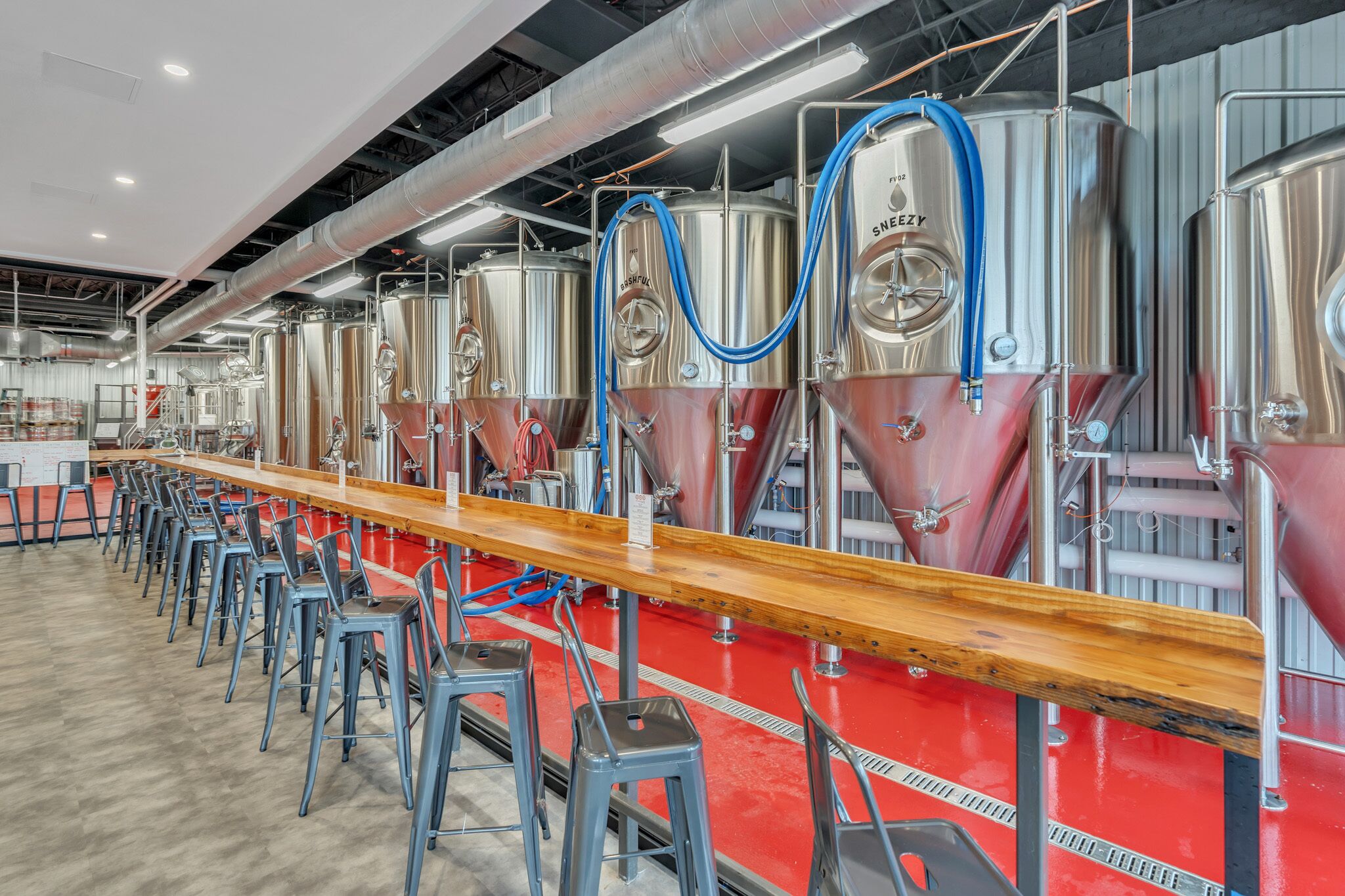 A brewery with stainless steel tanks and a long counter with stools.