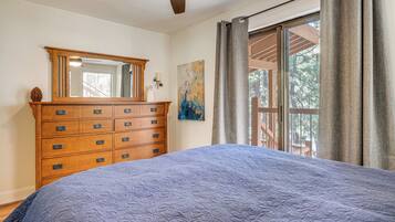 A bedroom with a large bed, a wooden dresser, a mirror, a painting, and a window with curtains.