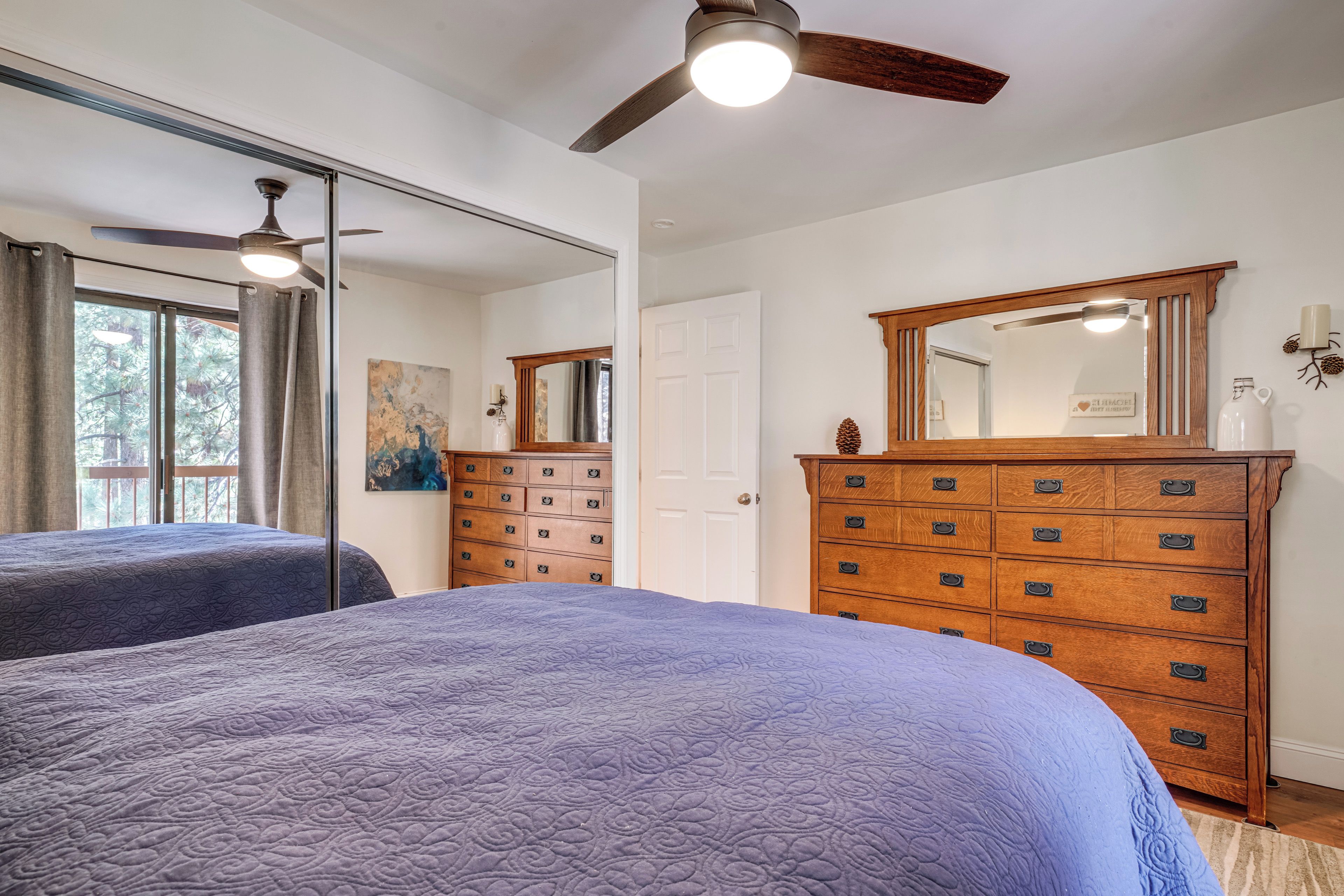 A bedroom with two beds, a wooden dresser, a ceiling fan, and a large mirror.