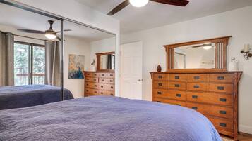 Une chambre avec deux lits, une commode en bois, un ventilateur de plafond et un grand miroir.