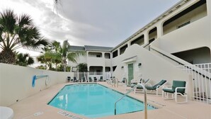 A pool area with lounge chairs, a staircase, and a building with multiple balconies. - South Padre Island Condo w/ Pool Access & Balcony! (South Padre Island)