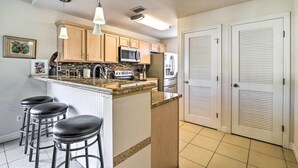 A kitchen with wooden cabinets, a microwave, a refrigerator, and a bar stool area. - South Padre Island Condo w/ Pool Access & Balcony! (South Padre Island)