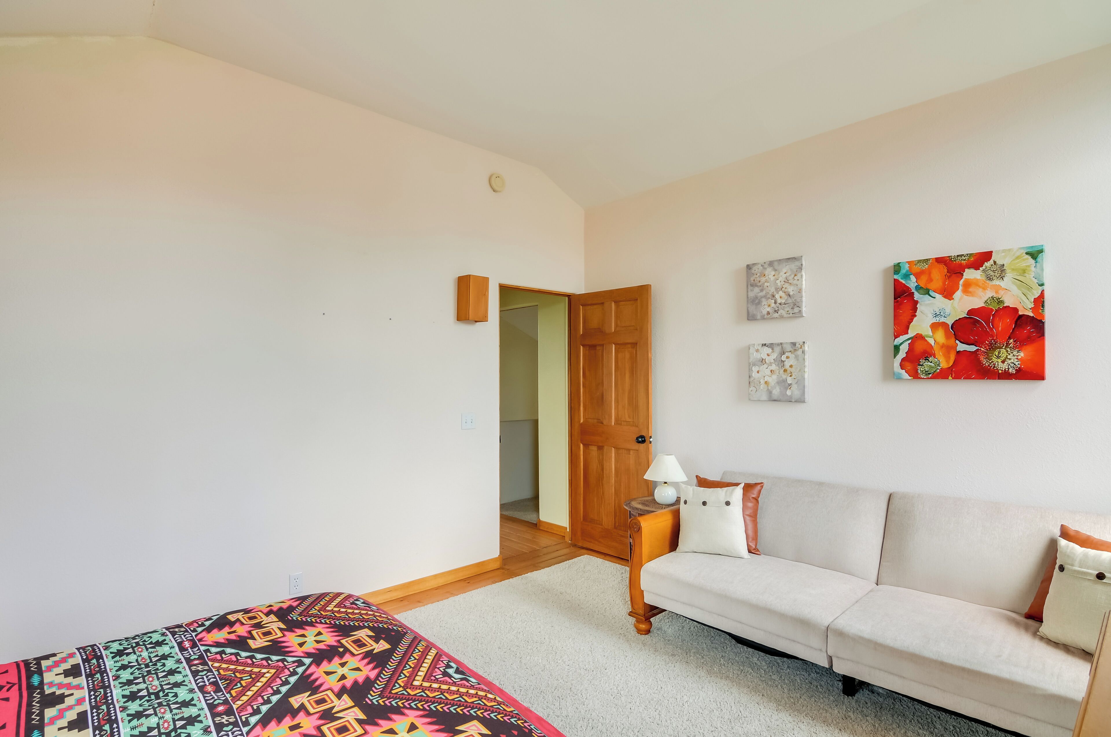 Um quarto com cama, sofá, porta de madeira e uma parede com duas molduras.
