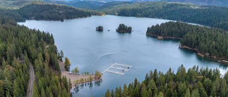 A lake surrounded by dense forest, a road curving through the trees, and a dock extending into the water.