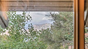 A view through a window with a wooden frame, featuring a mountain range in the background and various green plants in the foreground. - Elegant Mountain-view Condo < 1 Mi to Lifts! (Mammoth Lakes)