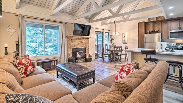 A spacious living room with a large sectional sofa, a fireplace, and a kitchen area with wooden cabinets and a stainless steel refrigerator. - Elegant Mountain-view Condo < 1 Mi to Lifts! (Mammoth Lakes)