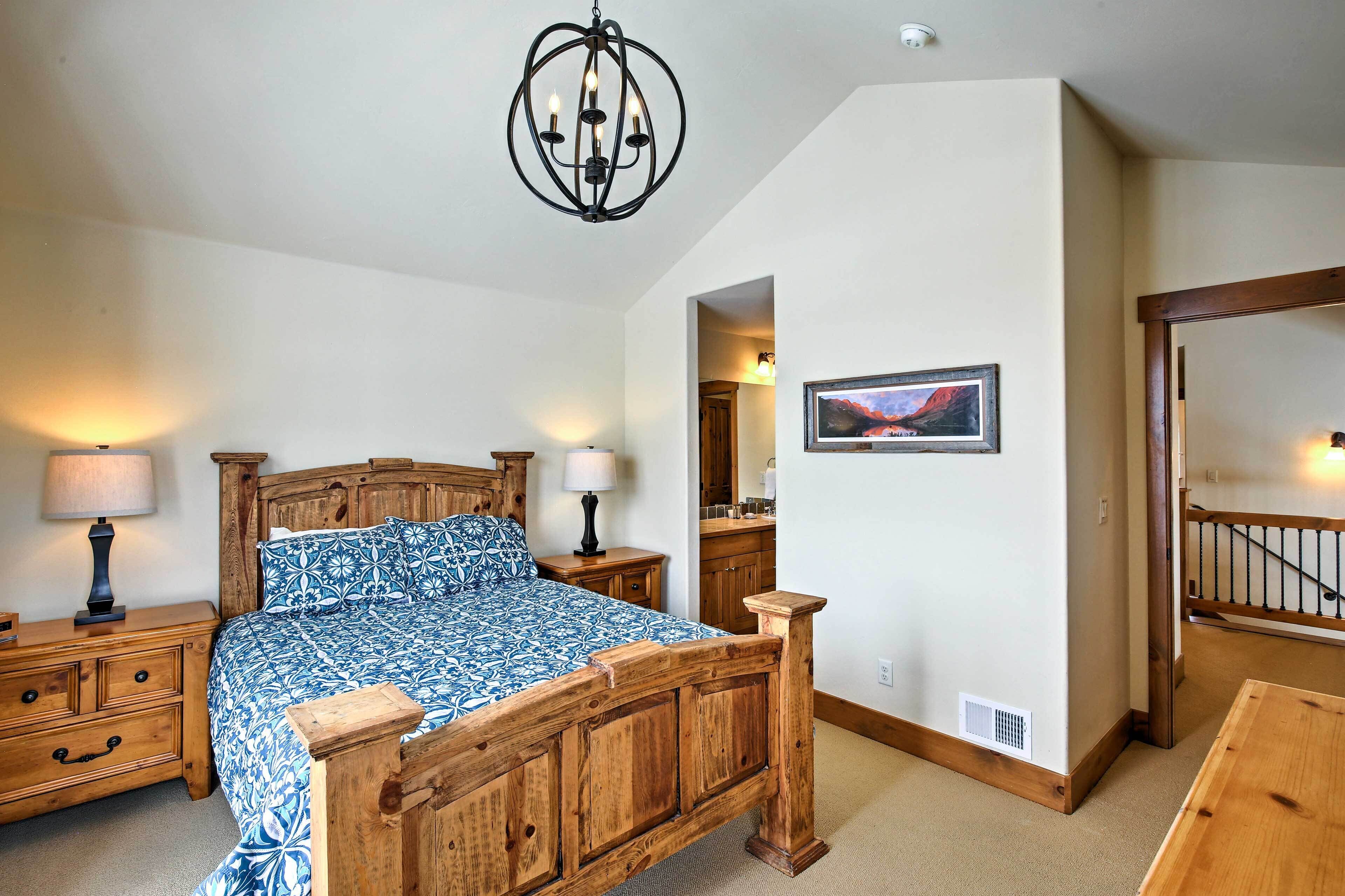 Une chambre à coucher avec un lit en bois, des tables de chevet avec des lampes, un lustre, un tableau encadré au mur et un escalier en bois.