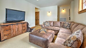 A living room with a large flat-screen TV on a wooden cabinet, a brown leather sofa, and a matching ottoman. - Mtn-view Gem w/ On-site Golf! 3 Mi to Granby Ranch (Granby)